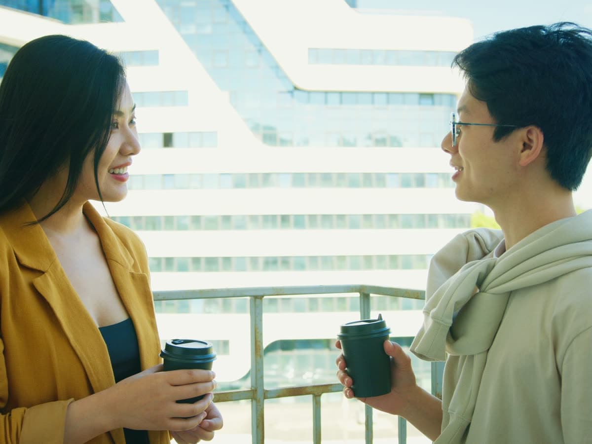 Two people talking over coffee on a balcony.